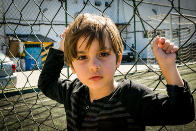 Portrait of boy standing against chainlink fence