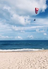 Person paragliding over beach against sky