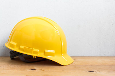 Close-up of yellow hardhat on table against white wall
