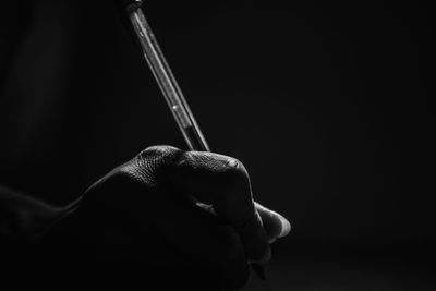 Close-up of hand holding cigarette against black background