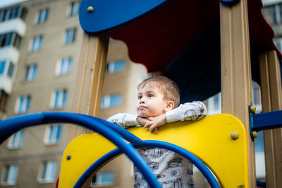 Low angle view of cute boy looking away while standing on outdoor play equipment