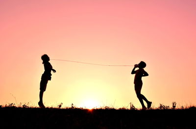 Silhouette of two people jumping against sky at sunset