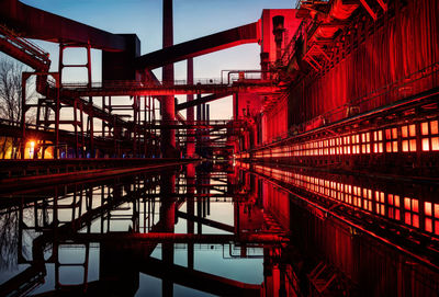 Bridge in illuminated factory against sky