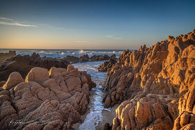 Rocks on beach against sky during sunset