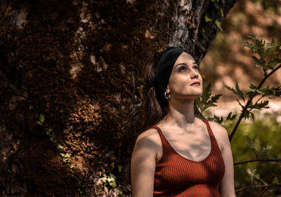 Portrait of young woman looking away against tree trunk