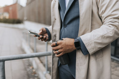 Midsection of male business professional surfing net through smart phone