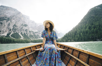 Woman looking away while sitting in rowboat over lake against mountains