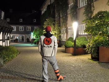 Rear view of man standing by illuminated street at night