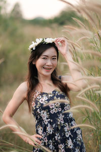 Portrait of smiling woman wearing flowers while standing on field