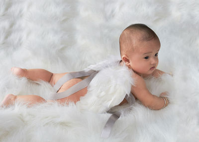 High angle view of cute baby girl lying over fur blanket on bed at home