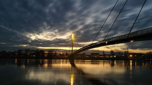 Bridge over river against cloudy sky at sunset