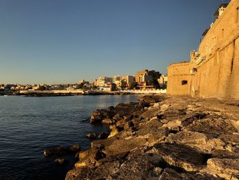 Buildings by sea against clear blue sky