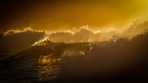 Scenic view of wave splashing in sea against sky during sunset