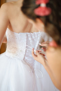 Midsection of woman tying wedding dress on bride
