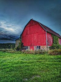 House on grassy field against cloudy sky