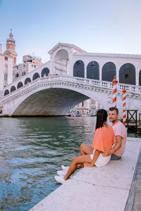 Full length of friends sitting on bridge against sky