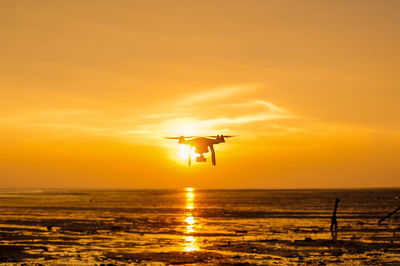 Silhouette bird flying over sea against sky during sunset