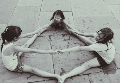 High angle view of happy sisters holding hands while sitting with legs apart on pavement