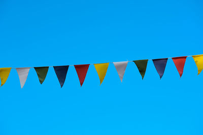 Low angle view of flags against clear blue sky