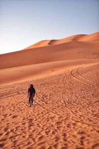 Woman walking on sand dune in desert against clear sky