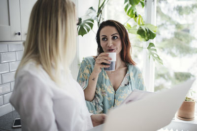 Businesswoman having drink while talking with colleague at home