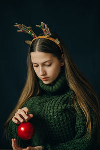 Teenager girl with christmas deer horns in a green sweater and red ball, sad
