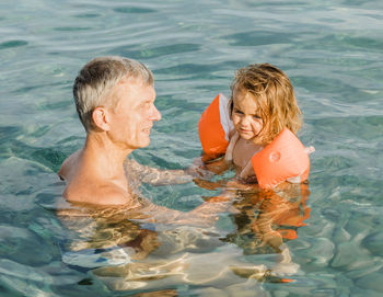 Grandfather swimming with granddaughter in sea