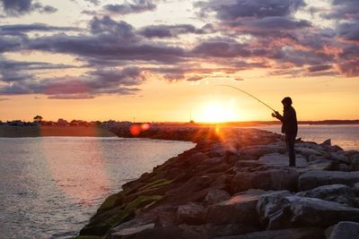 Silhouette man fishing in sea against sky during sunset