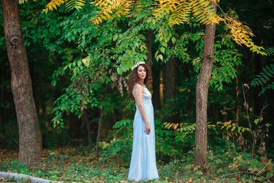 Portrait of woman standing by tree in forest