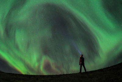 Low angle view of man using flashlight towards aurora borealis in sky