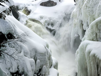 Small waterfalls cascading into narrow river with banks covered in snow and icicles, dorwin falls