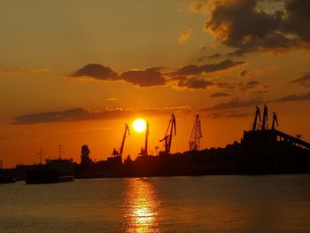 Yellow sun in orange sunset in cloudy sky behind the harbor cranes.