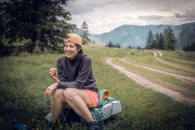 Smiling young woman sitting on field against mountain view