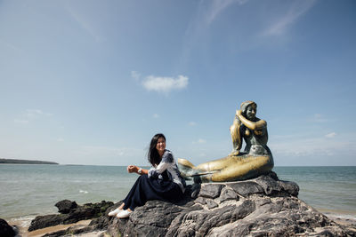 People sitting on rock by sea against sky