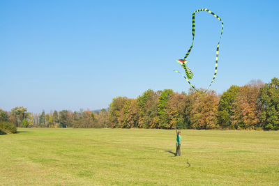 Boy flying kite on field against clear blue sky