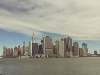 City at waterfront against cloudy sky