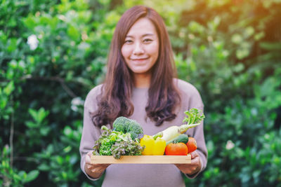 Portrait of smiling woman holding food against plants