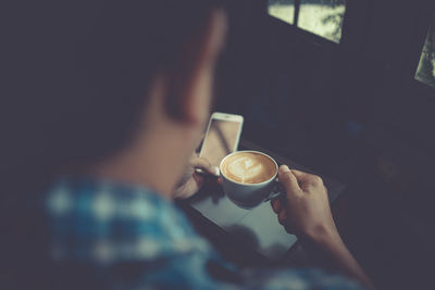 Rear view of man holding coffee cup while using smart phone in cafe