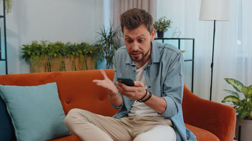 Young man using mobile phone while sitting on sofa at home