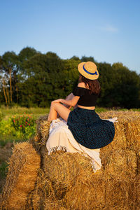 Rear view of woman sitting on field against sky