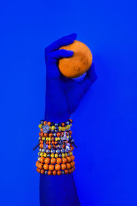 Close-up of hand holding an orange against blue background