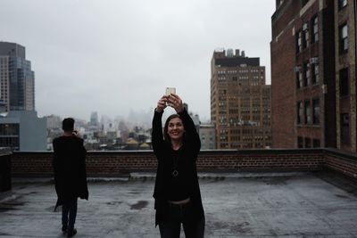 Smiling woman photographing while standing on building terrace in city