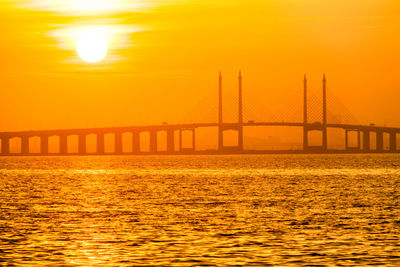 Bridge over sea against orange sky