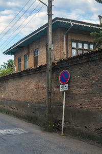 Road sign on street by building against sky