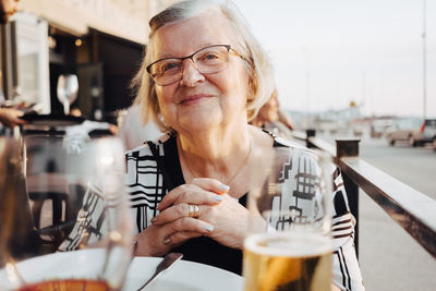 Smiling senior female tourist sitting with hands clasped at restaurant