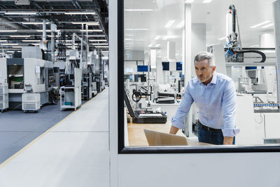 Confident businessman looking through glass at factory