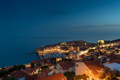 High angle view of illuminated city by sea against sky