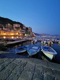 Boats moored at harbor by buildings against clear blue sky