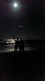 Silhouette friends standing on beach at night