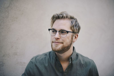 Thoughtful male computer programmer looking away against beige wall in office